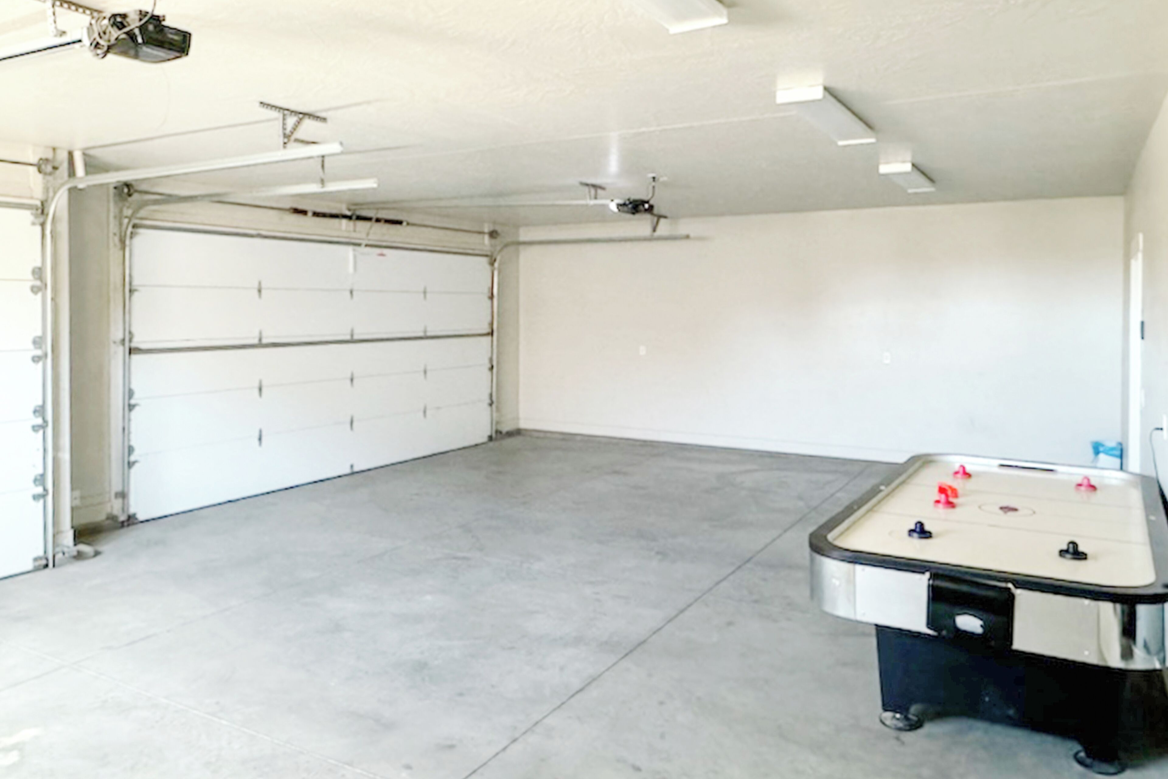 A spacious garage with a foosball table, a ceiling fan, and a garage door.