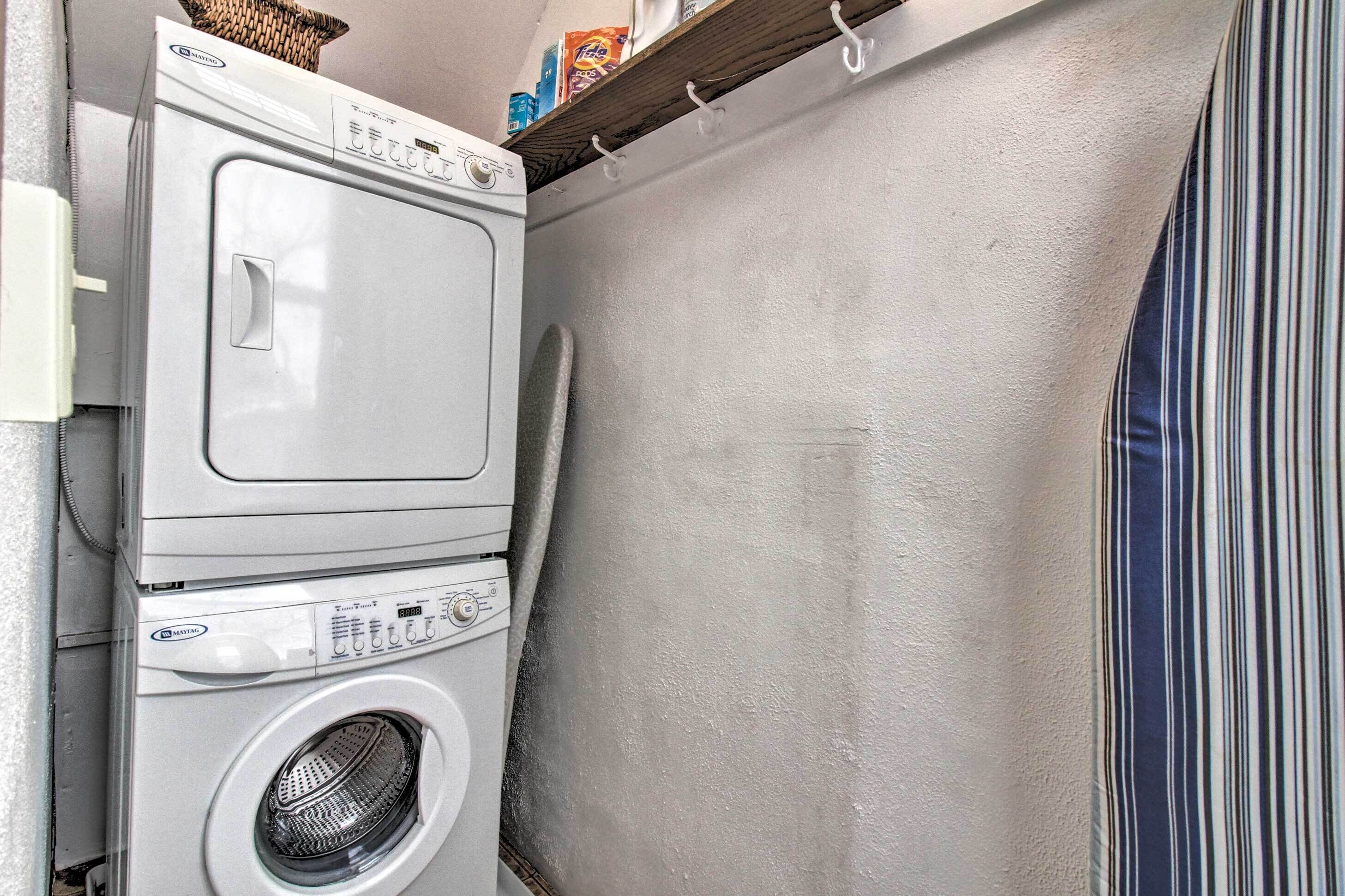 Une petite buanderie équipée d’un lave-linge et d’un sèche-linge superposés, d’une étagère contenant le matériel de lessive et d’un rideau à rayures.