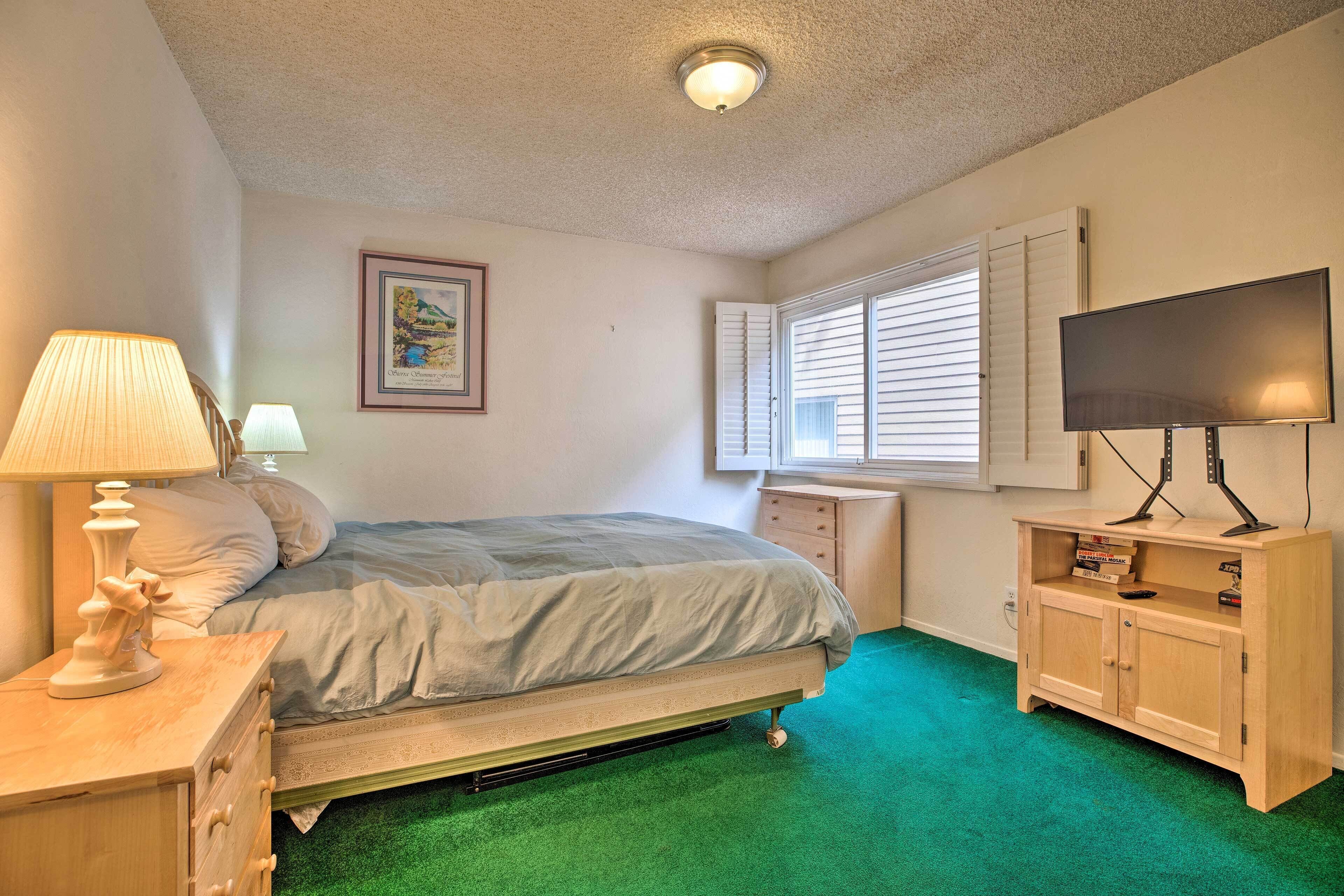 A bedroom with a bed, a desk, a television, and a window with blinds.