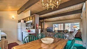 A cozy living area with a wooden dining table, green chairs, a sofa, and a television.
