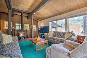 A cozy living room with a wooden ceiling, a fireplace, a sofa, a coffee table, and a television.