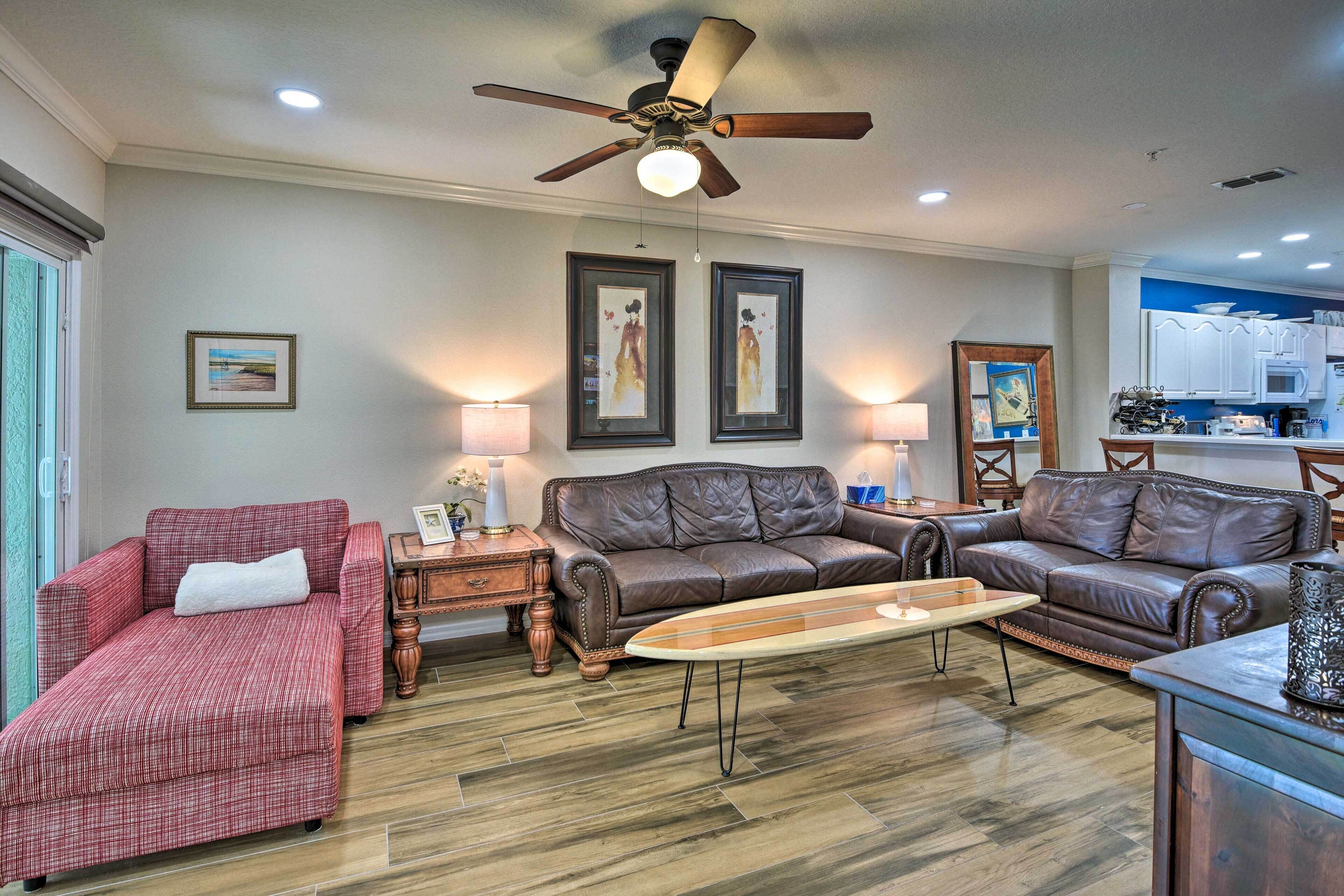 A living room with a brown leather sofa, a red plaid sofa, a wooden coffee table, and a ceiling fan.