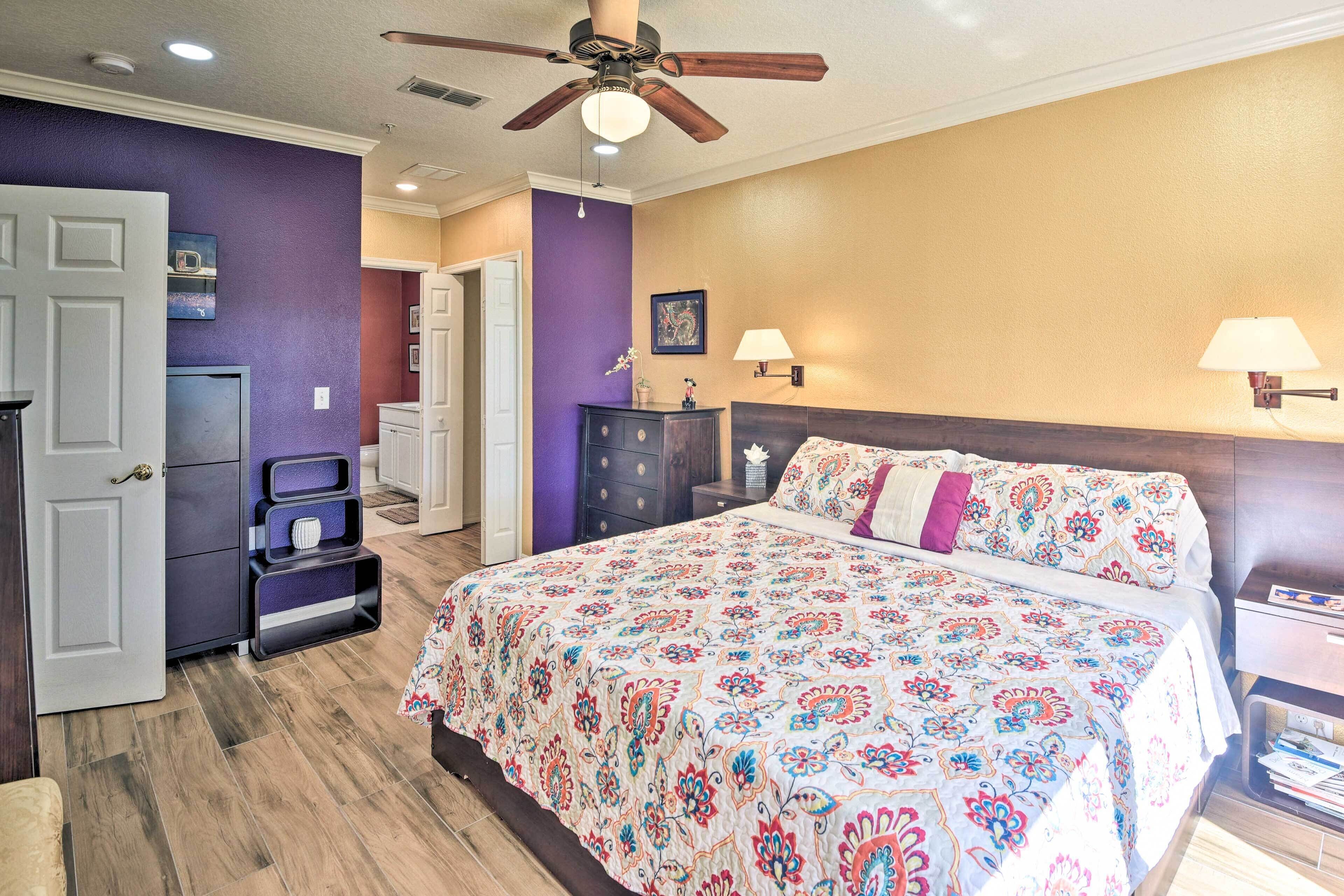 A bedroom with a large bed, a ceiling fan, a dresser, and a nightstand.