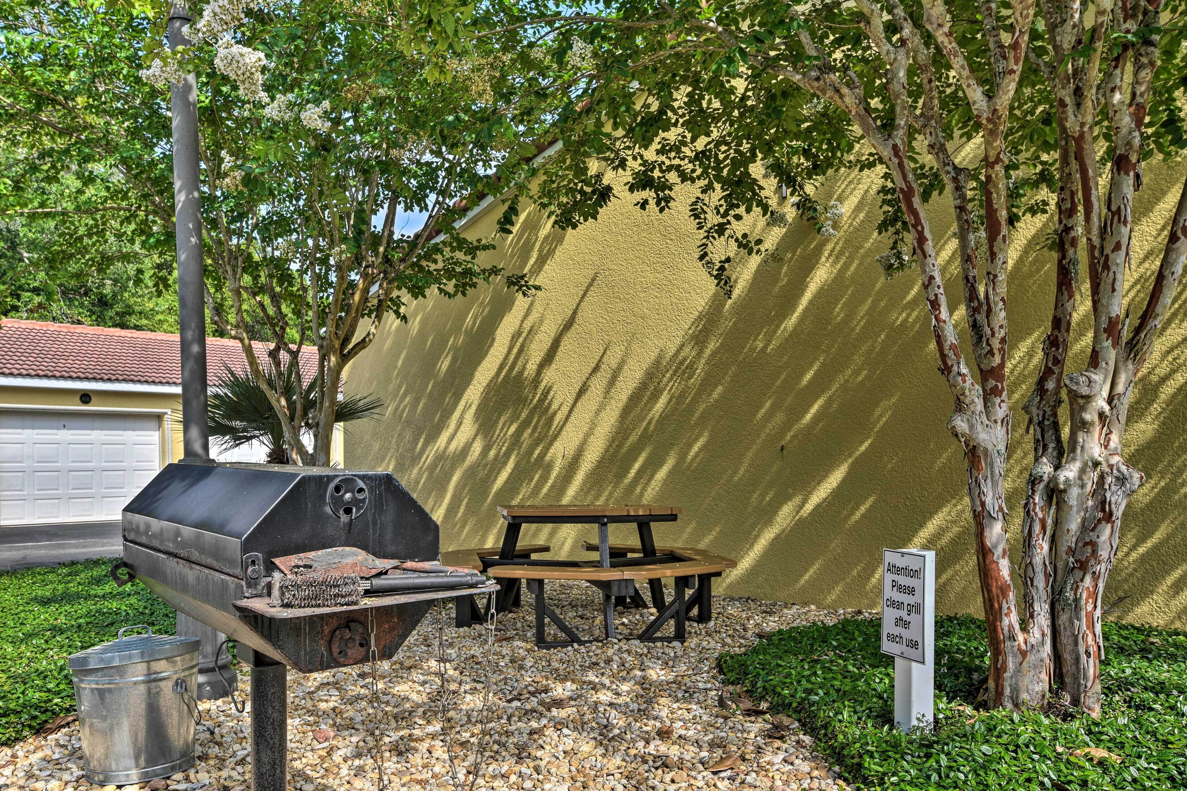 An outdoor barbecue area with a grill, picnic table, and a sign instructing to clean the grill after use.