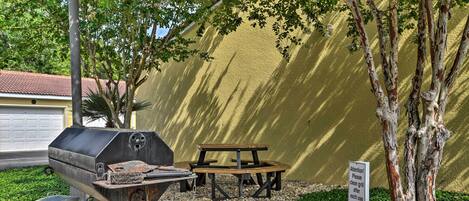 An outdoor barbecue area with a grill, picnic table, and a sign instructing to clean the grill after use.