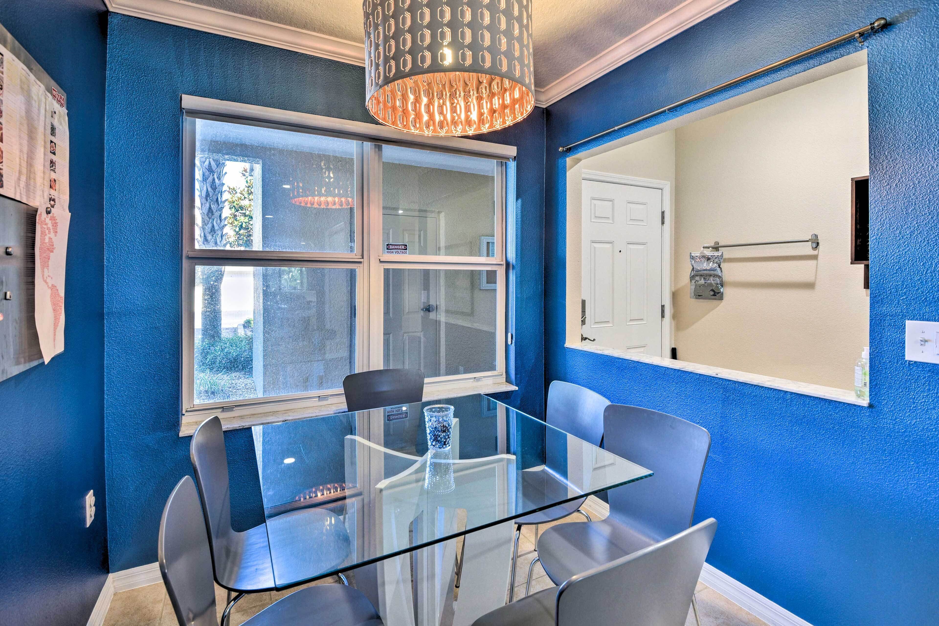 Una habitación con mesa y sillas de vidrio, una ventana con vistas y una puerta con perchero para toallas.