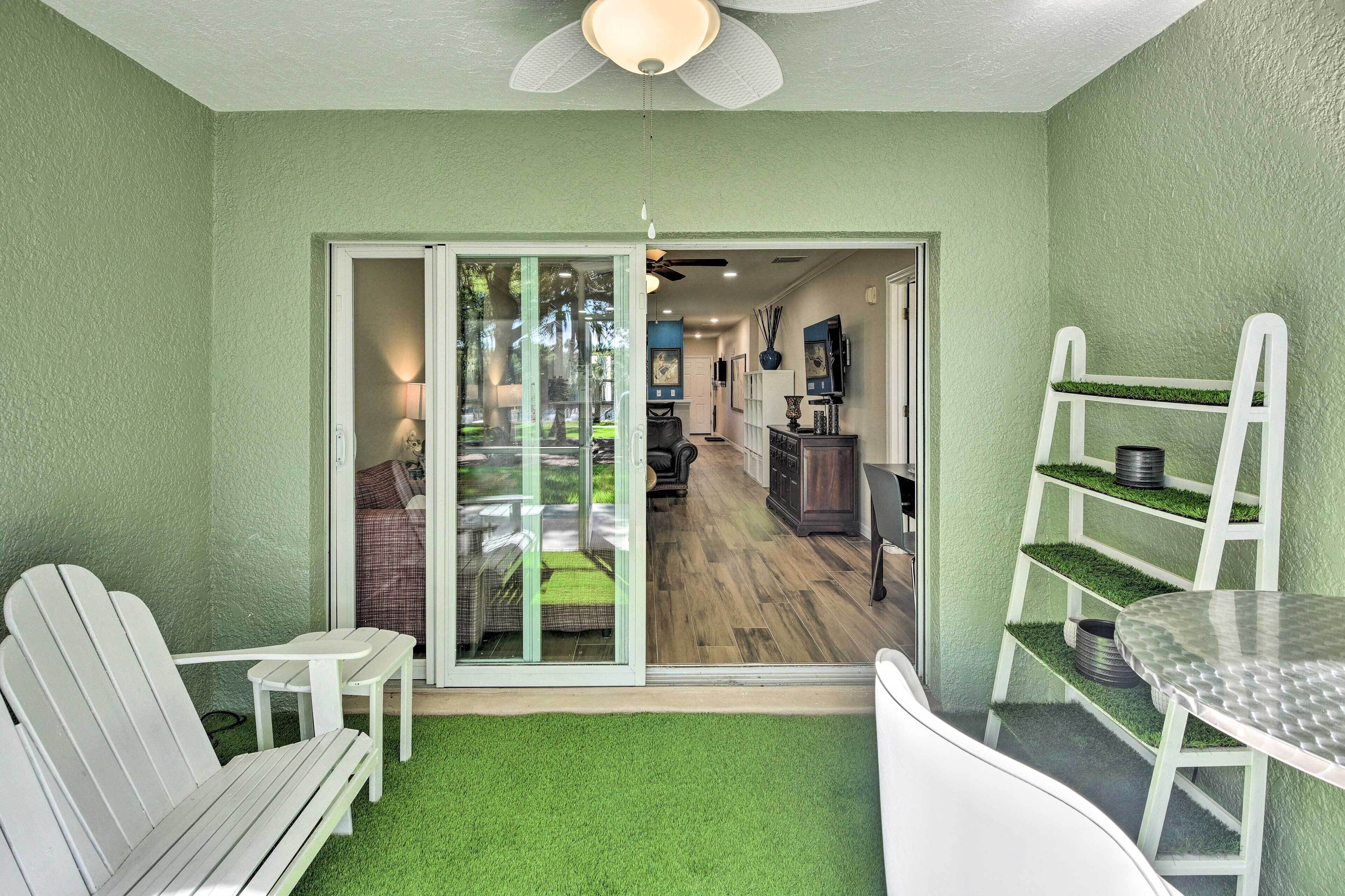 A room with a sliding glass door leading to a patio area with a lawn, a ceiling fan, and a dining table with chairs.