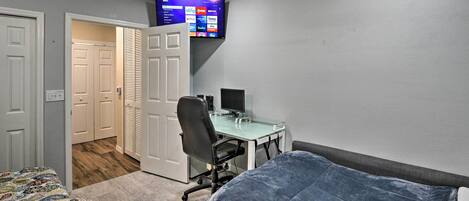 Una camera da letto con un letto, una scrivania, una sedia, una TV fissata al muro e una porta che dà su un'altra stanza.