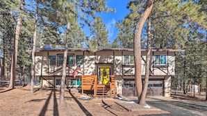 A two-story building with a garage, surrounded by tall pine trees. - Scenic Woodland Park Cottage w/ Deck + Grill! (Woodland Park)