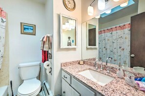 A bathroom with a white toilet, a sink with a mirror, and a shower curtain with floral patterns. - Scenic Woodland Park Cottage w/ Deck + Grill! (Woodland Park)