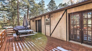 A wooden deck with picnic tables and a barbecue area, surrounded by tall trees. - Scenic Woodland Park Cottage w/ Deck + Grill! (Woodland Park)