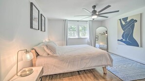 A bedroom with a bed, a ceiling fan, a bedside lamp, a window, and artwork on the walls. - Artsy Upstate Getaway w/ Huge Private Yard! (Whitesboro)