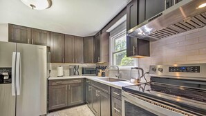 A modern kitchen with dark wood cabinets, stainless steel appliances, and a large window providing natural light. - Artsy Upstate Getaway w/ Huge Private Yard! (Whitesboro)