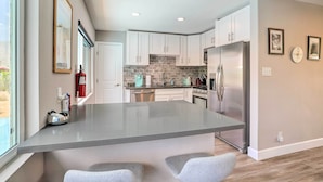 A modern kitchen with white cabinets, a central island, and a stainless steel refrigerator. - Palm Springs Retreat w/ Private Pool & Spa! (Palm Springs)