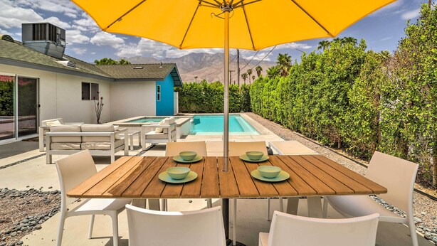 An outdoor patio with a wooden table, white chairs, and a yellow umbrella. - Palm Springs Retreat w/ Private Pool & Spa! (Palm Springs)