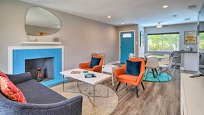 A modern living room with a fireplace, orange armchairs, a gray sofa, and a dining area with a blue door in the background. - Palm Springs Retreat w/ Private Pool & Spa! (Palm Springs)
