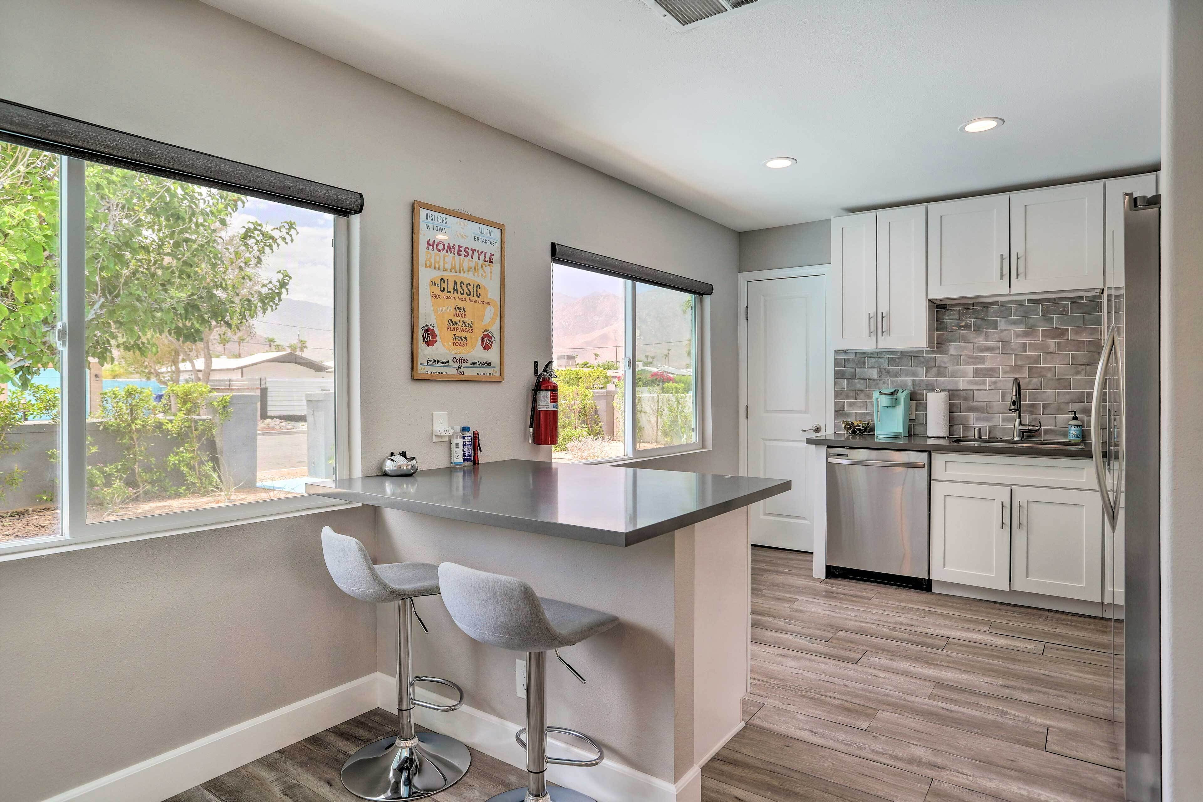 A modern kitchen with a central island, bar stools, and a view of the outdoors.