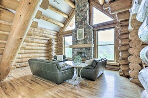 A log cabin interior with a stone fireplace, leather sofas, and large windows offering a mountain view. - Mountain Retreat w/ Deck: Ski, Soak, Golf & Hike! (Glenwood Springs)