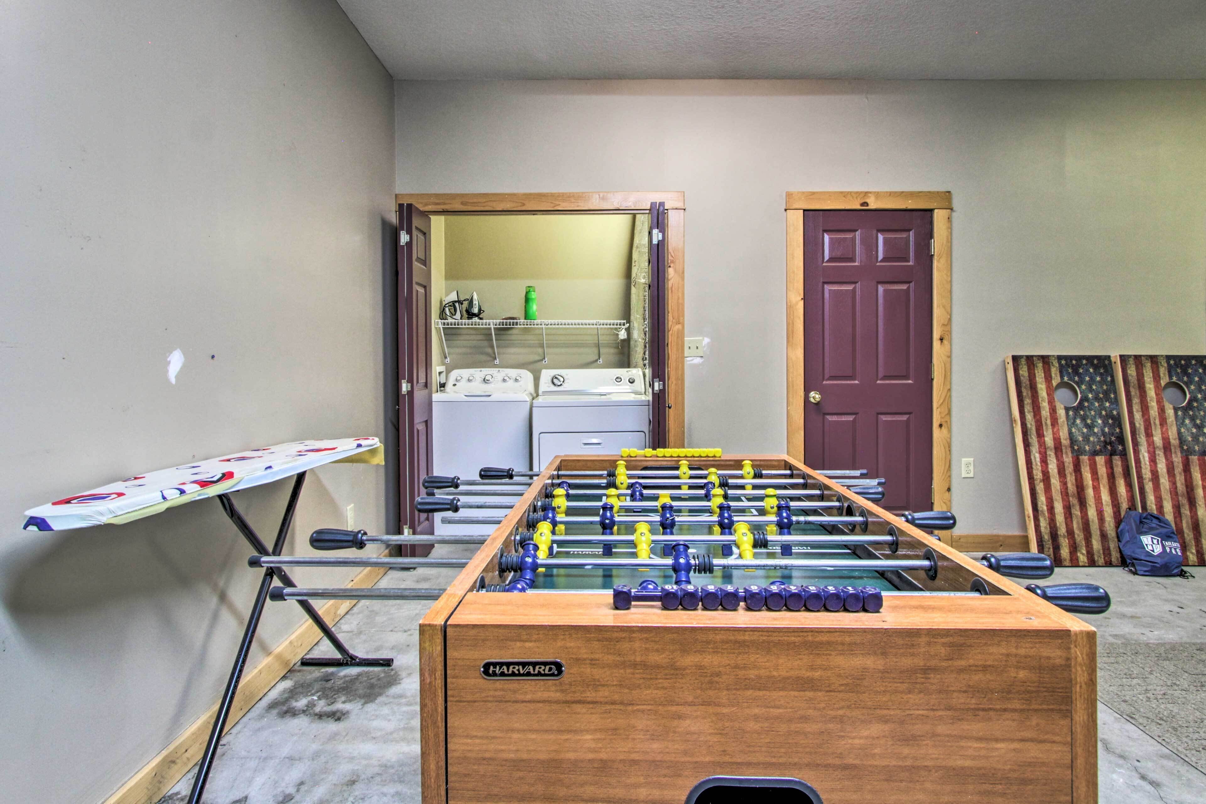 A room with a foosball table, an ironing board, and a kitchenette in the background.