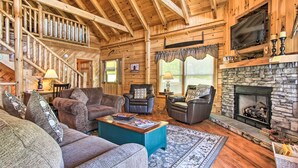 L’intérieur d’une cabane en rondins, avec une cheminée, un escalier en bois et un salon confortable doté de canapés en cuir et d’une table basse.