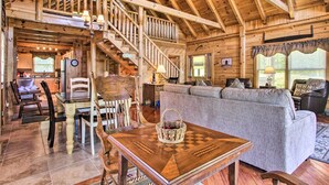 Un vaste salon agrémenté d’un escalier en bois, un coin repas avec une table et des chaises en bois, et un espace salon confortable avec un canapé et des fauteuils.