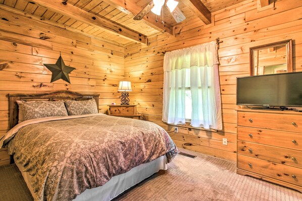 A wooden cabin bedroom with a bed, nightstand, lamp, TV, and a star decoration on the wall. - Idyllic Sevierville Cabin: Deck + Smoky Mtn View! (Sevierville)