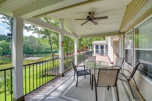 A covered outdoor area with a table and chairs, a ceiling fan, and a view of a green landscape. - Lakefront Arkansas Home w/ Dock & Sunroom (Hot Springs)