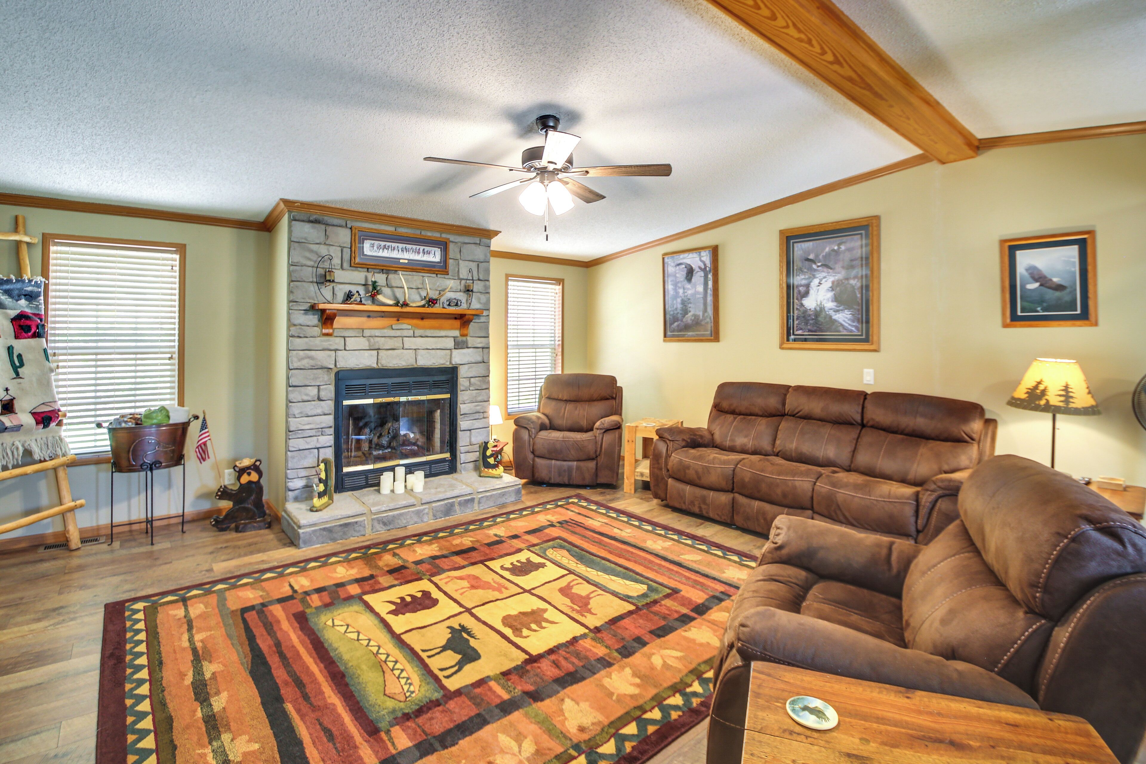 A living room with a fireplace, leather sofas, a rug, and a ceiling fan.