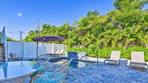 A pool area with a glass table, wicker chairs, and lounge chairs.