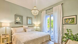 A bedroom with a large bed, bedside lamps, a chandelier, and a view of the outdoors through a sliding door.