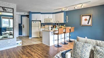 A modern living space with a kitchen, a dining area, and a seating area with a sofa and bar stools.