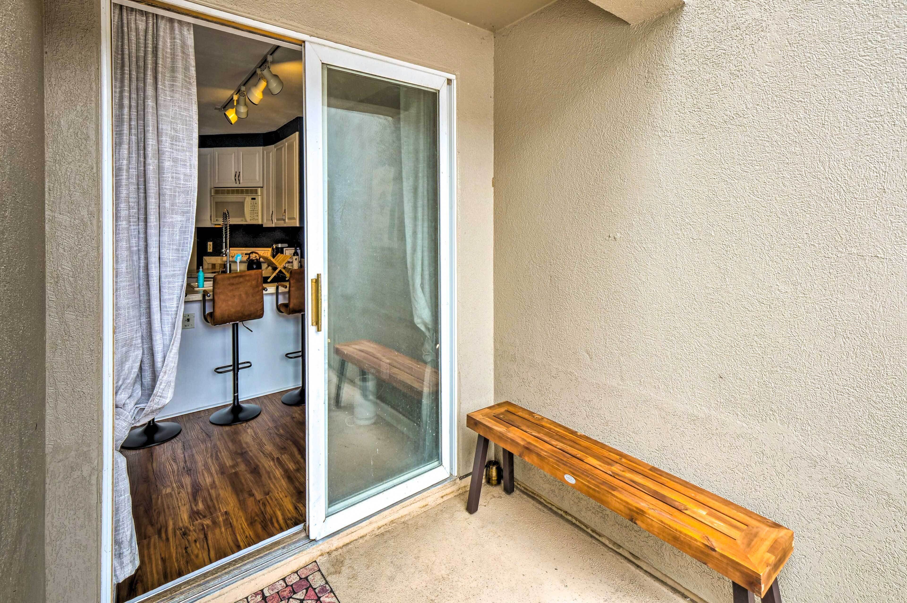 Una puerta corrediza de vidrio da a un área de cocina con un banco y una mesa afuera.