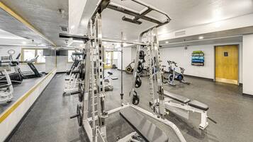 Un gimnasio con diferentes máquinas de ejercicio, un espejo en la pared y una puerta al fondo.