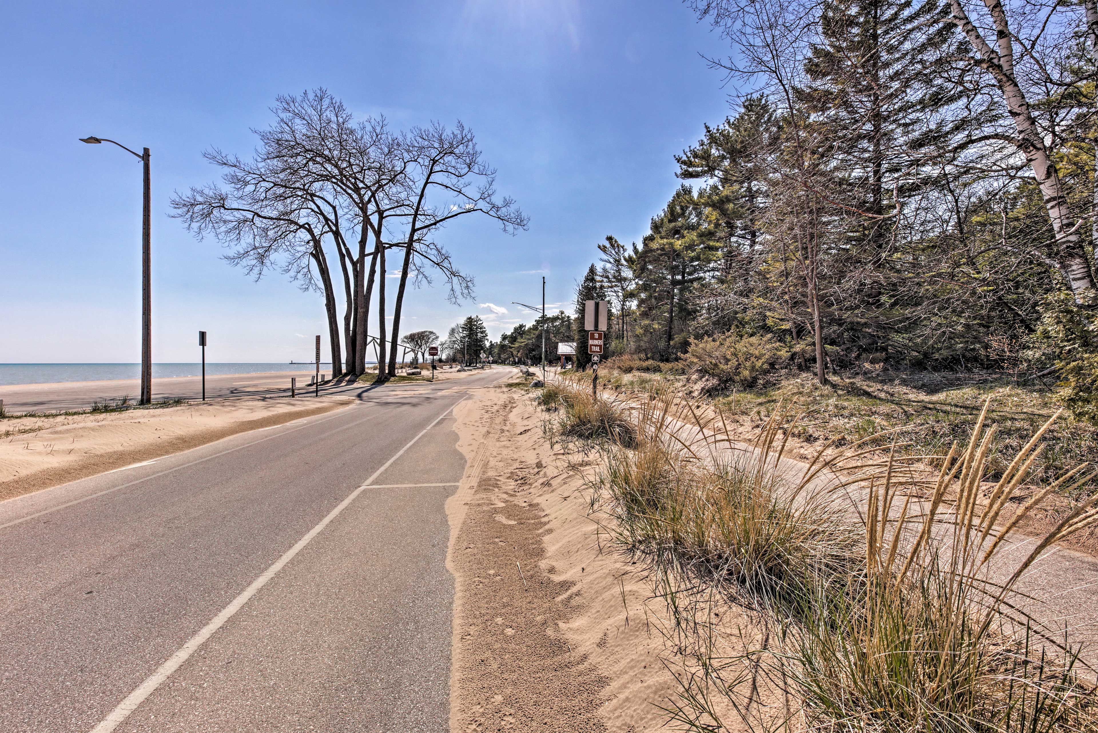 A coastal road with a sandy beach on one side and a forested area on the other.