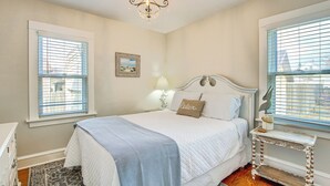A bedroom with a bed, a nightstand, a lamp, a chandelier, and a window with blinds. - 'ania's Retreat' w/ Deck: Walk to Lake Michigan! (Two Rivers)