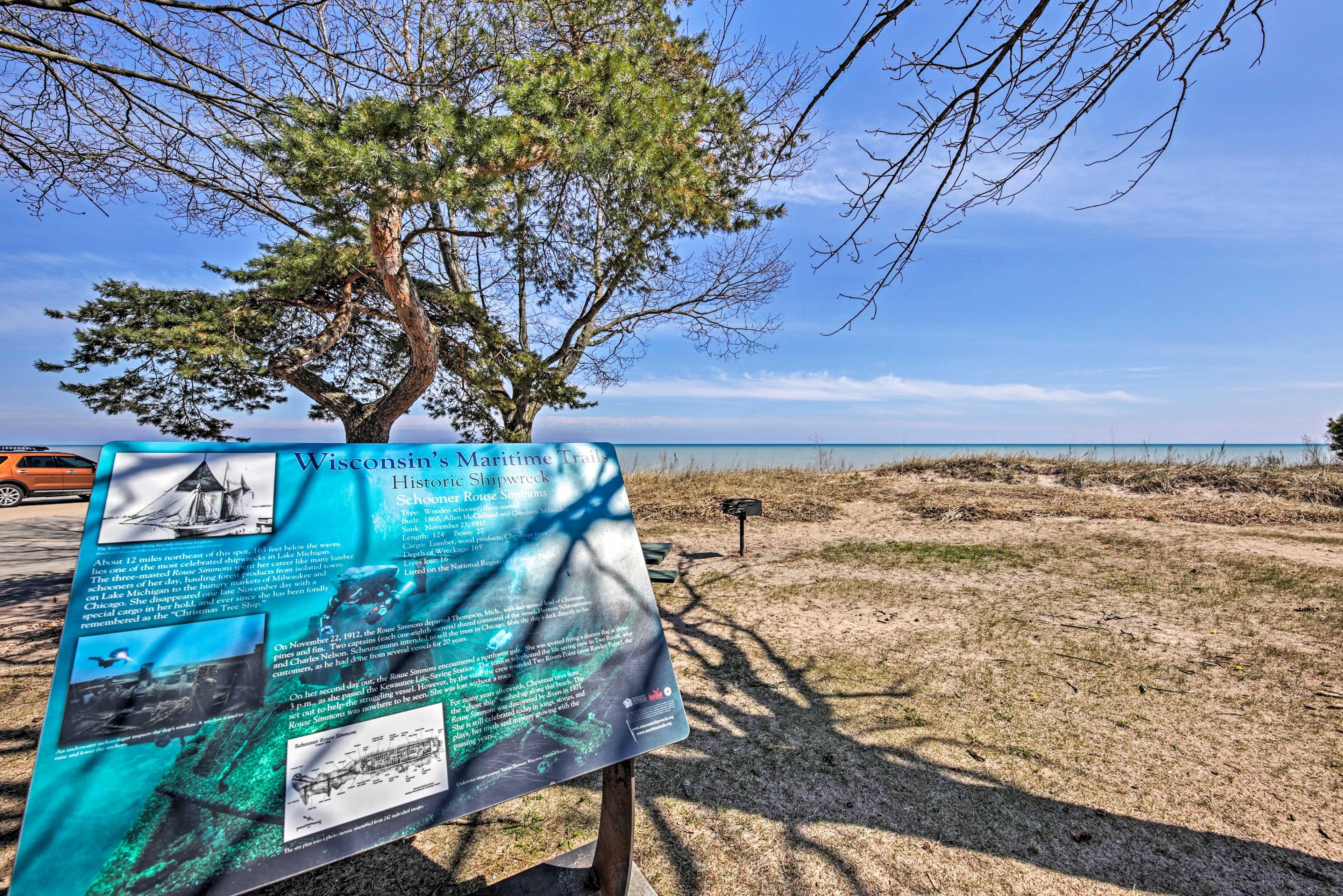 A historical shipwreck information sign by the beach with a tree in the foreground.