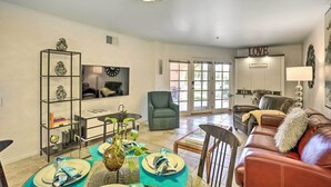 A living room with a brown leather sofa, a teal coffee table, and a glass-top dining table with plates and napkins. - Condo w/ Patio, Walk to Downtown Palm Springs! (Palm Springs)
