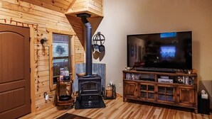 Ein gemütliches Wohnzimmer mit Holzvertäfelung, einem großen Flachbildfernseher, einem eingebauten Holzofen und einer Holz-Unterhaltungsanlage.