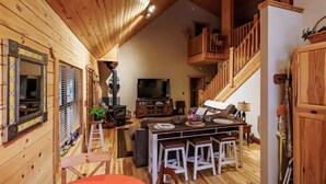 Ein gemütliches Holzambiente mit einer zentralen Sitzgruppe, einem Kamin und einer Treppe, die in eine obere Etage führt.