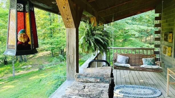 Eine Holzterrasse mit einer Bank und einem Teppich, umgeben von viel Grün.