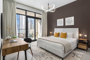 A modern bedroom with a large bed, a desk, and a view of the city through large windows.