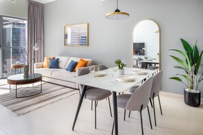 A modern living room with a dining area, a sofa with cushions, a coffee table, a dining table set with plates and glasses, a potted plant, and a large mirror.
