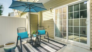 Eine Terrasse mit zwei Stühlen, einem Tisch, einem blauen Sonnenschirm und einem Blumentopf.