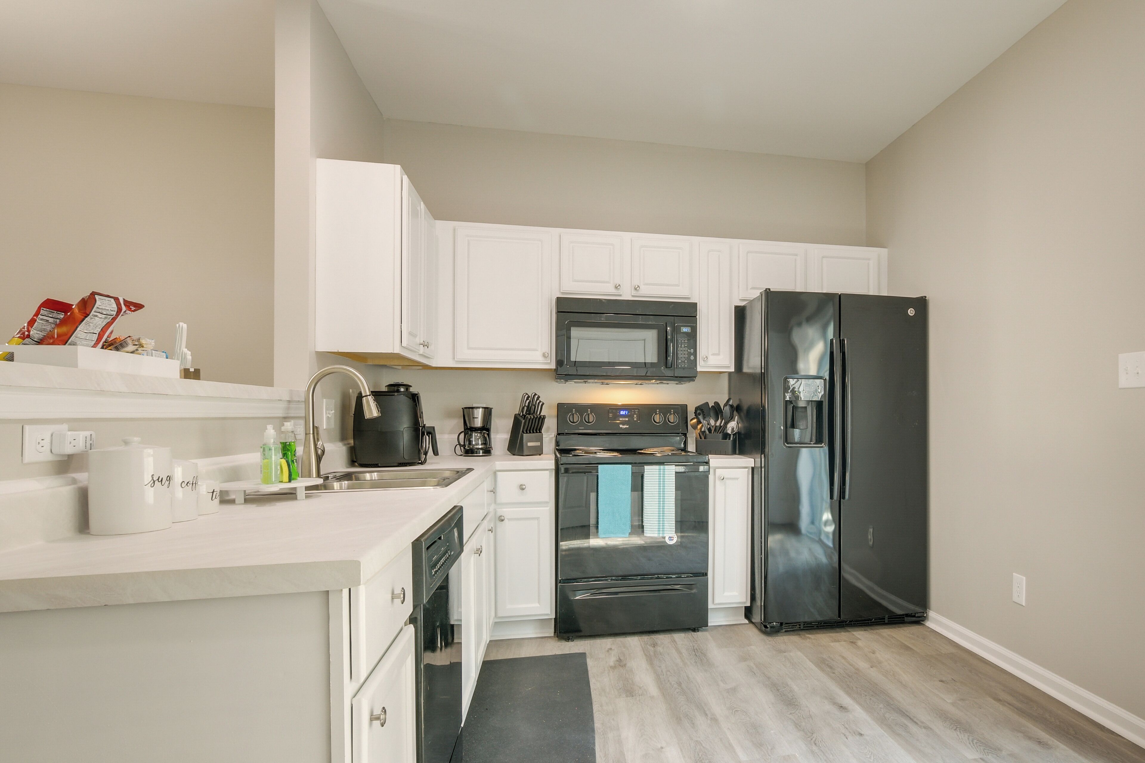 A modern kitchen with white cabinets, a black refrigerator, a microwave, an oven, and a coffee maker.