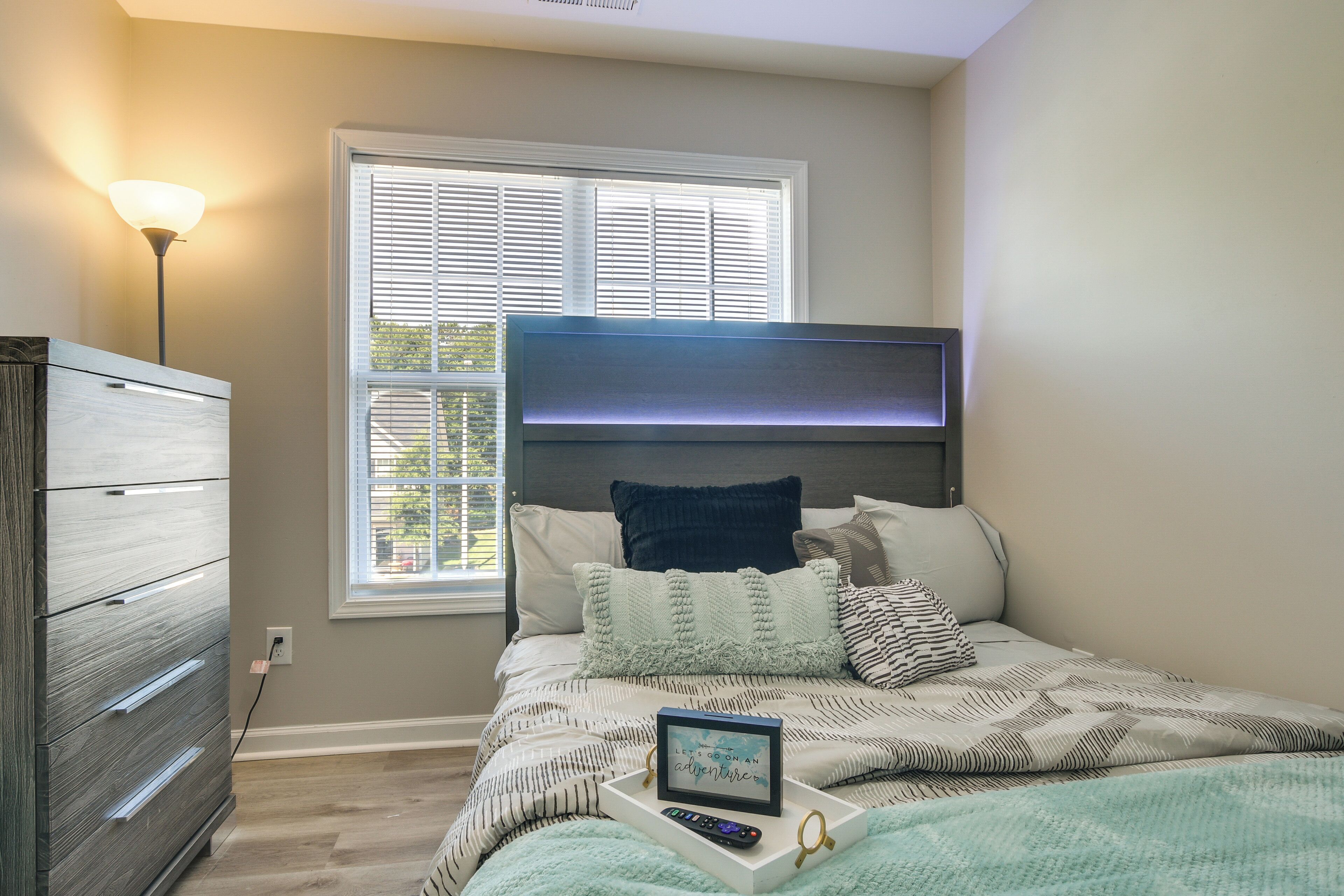 A bedroom with a bed, a dresser, a nightstand, and a window with blinds.