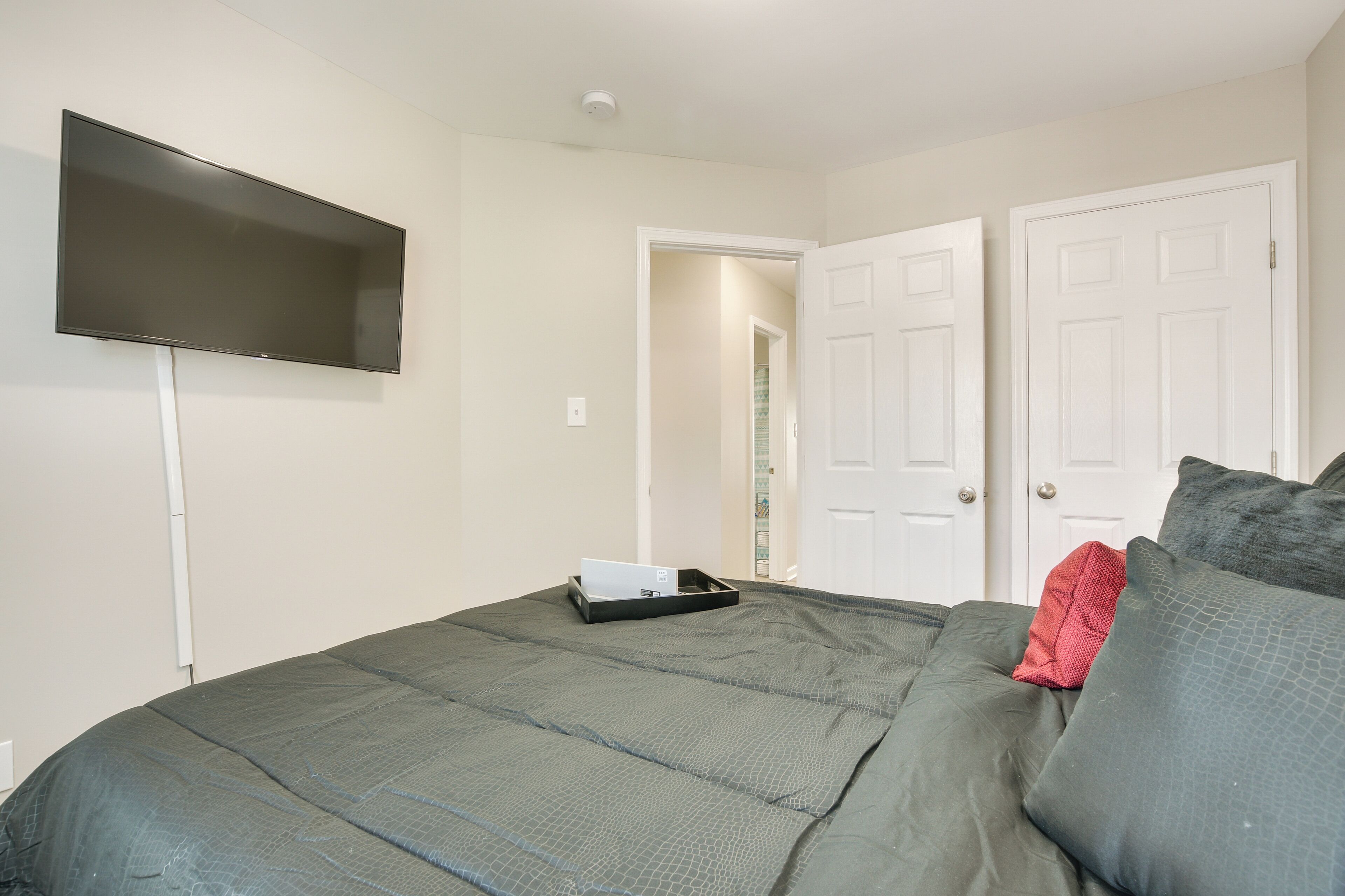 A bedroom with a bed, a flat-screen TV mounted on the wall, and a door leading to another room.