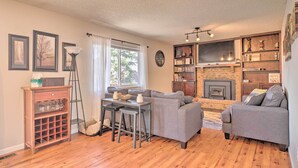 A living room with a fireplace, a sofa, a coffee table, and a bookshelf. - Lovely Colorado Springs Home: Mtn Views & Hot Tub! (Colorado Springs)