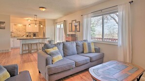 A modern living room with a grey sofa, a wooden coffee table, and a kitchen in the background. - Lovely Colorado Springs Home: Mtn Views & Hot Tub! (Colorado Springs)