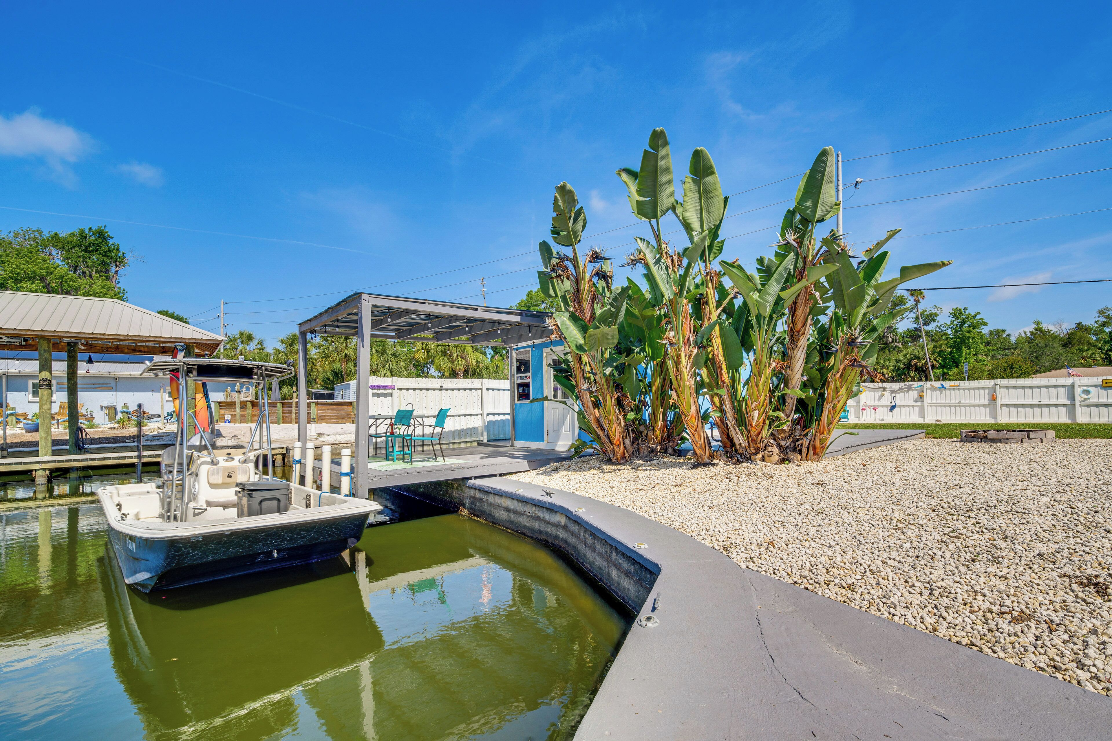A boat docked at a marina with a covered seating area and banana plants nearby.
