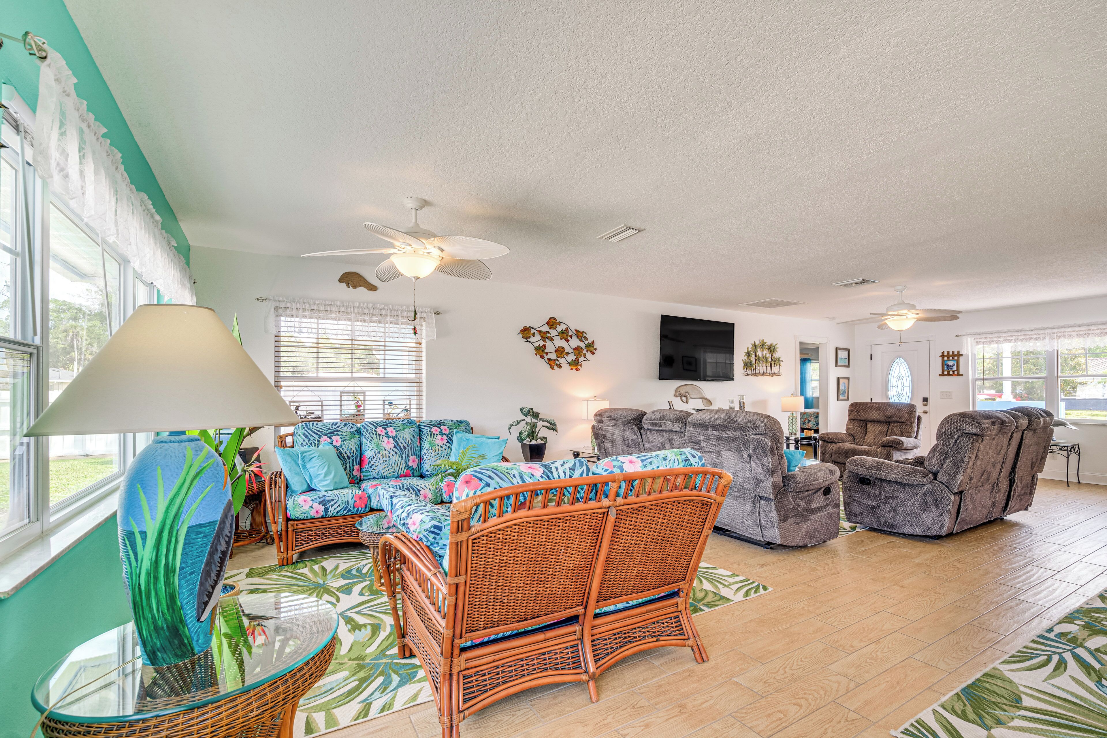 A spacious living room with wicker furniture, a large window, and a ceiling fan.